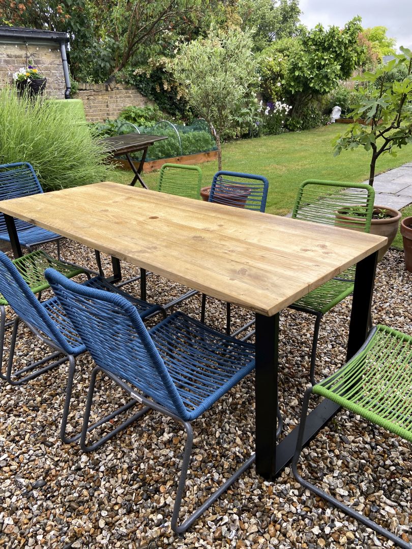 Outdoor garden setting with a wooden table and colorful chairs on a gravel surface.