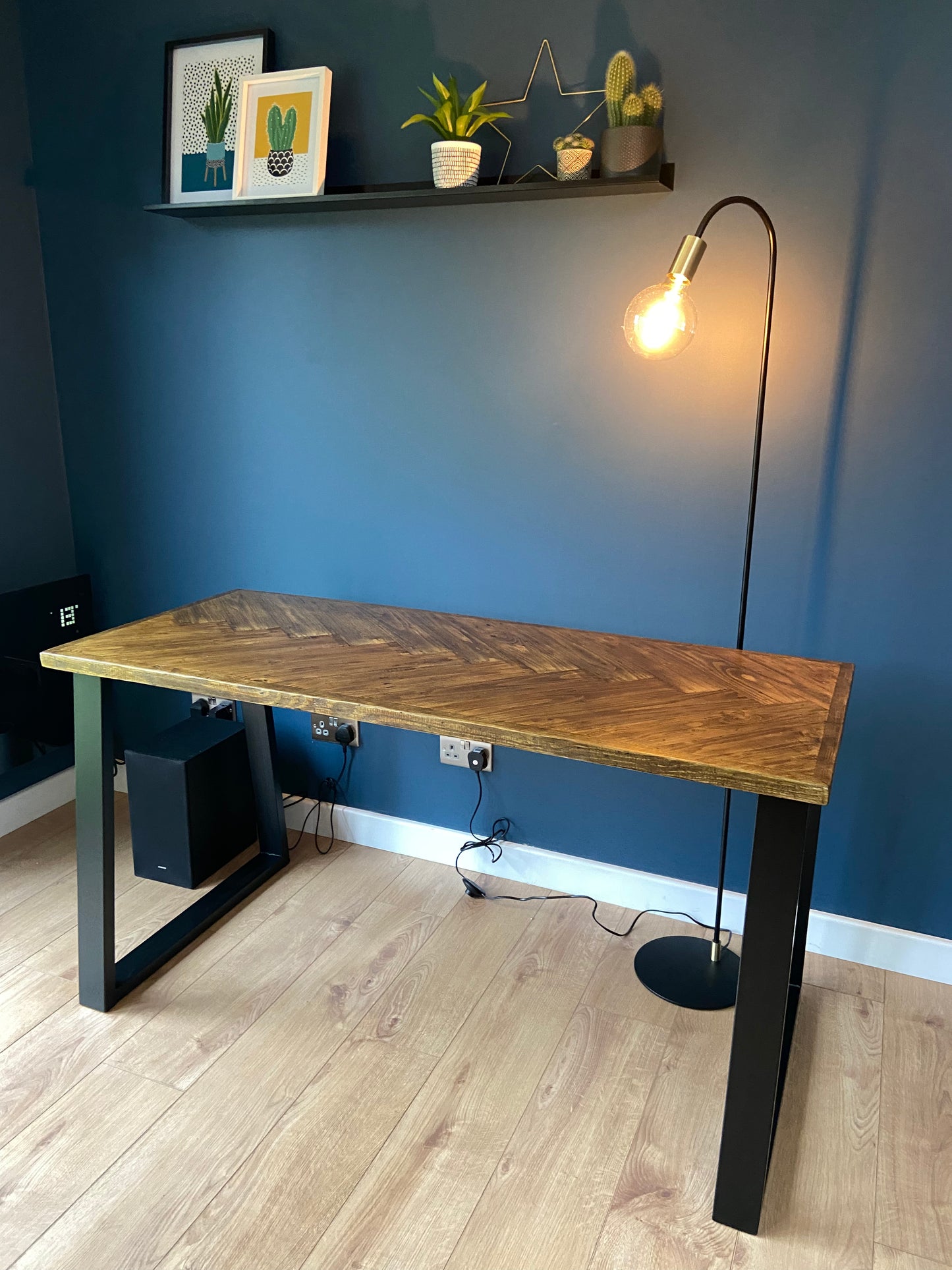 Reclaimed wood desk with herringbone top and black industrial metal legs, featuring a smooth wax finish and natural wood variations