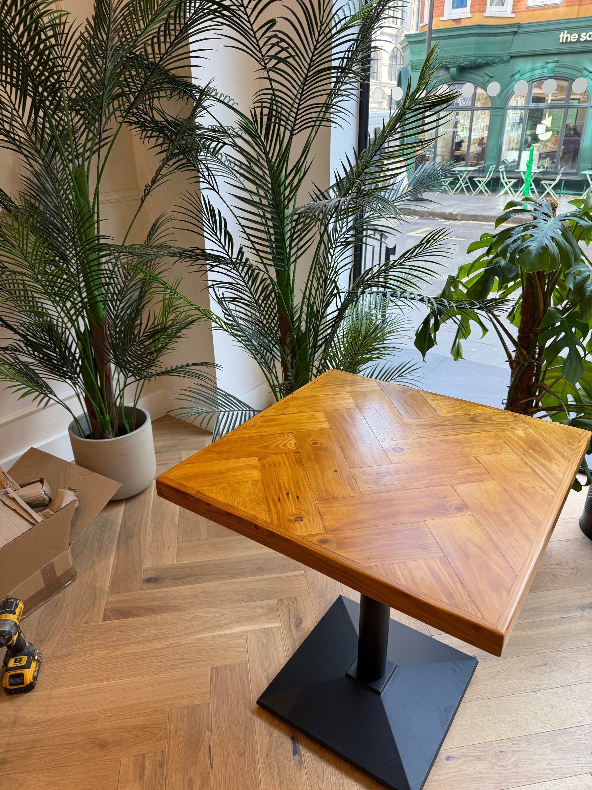 Handmade square bistro table with double herringbone reclaimed wood top and black cast iron pedestal base, finished with natural wax