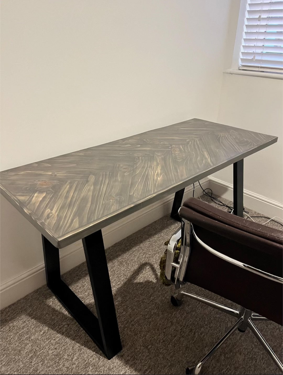 Reclaimed wood desk with herringbone top and black industrial metal legs, featuring a smooth wax finish and natural wood variations