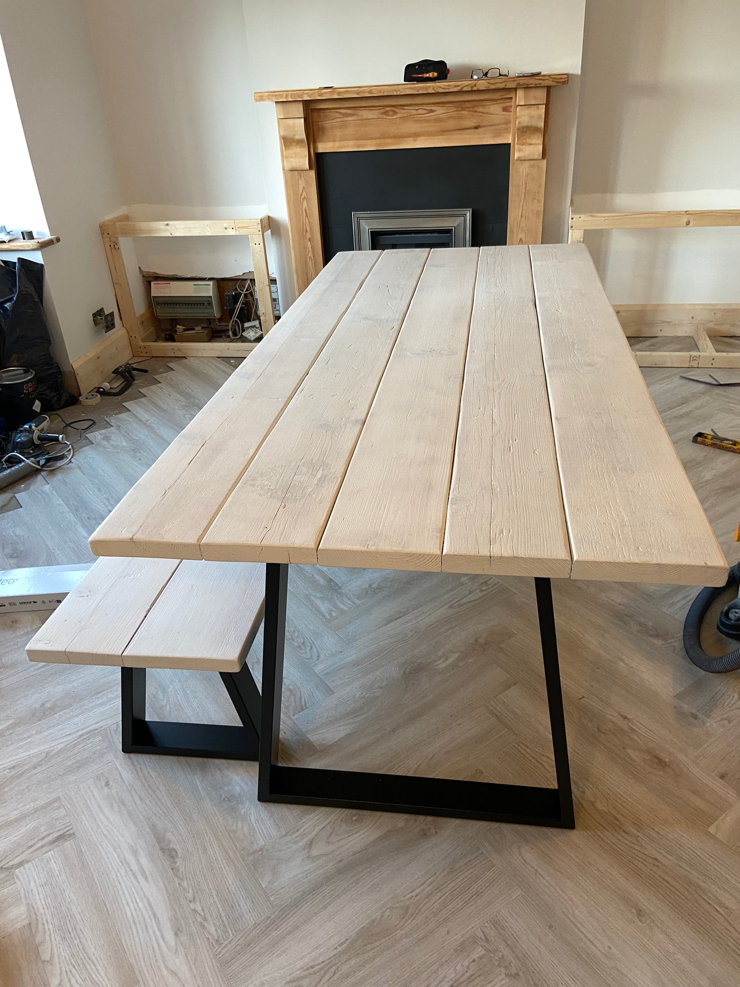 Wooden dining table with black metal legs in a room with a fireplace.